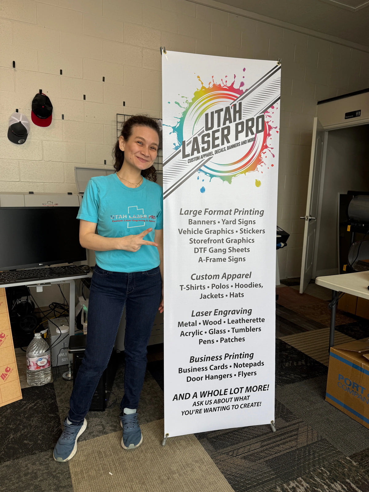 Person standing beside a tall Utah Laser Pro banner inside the print shop.