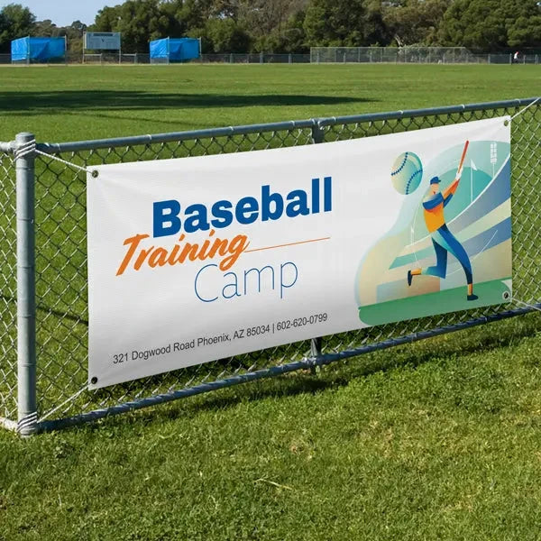 Baseball Training Camp banner mounted on a chain-link fence beside a playing field.