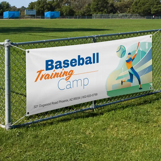 Custom Baseball Training Camp banner attached to a chain-link fence beside a playing field.
