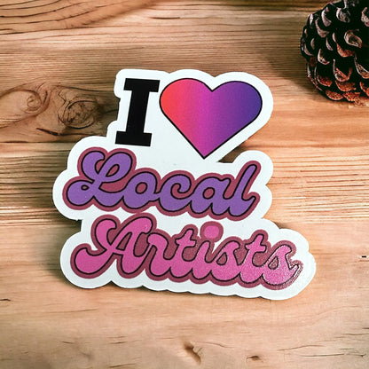Die-cut I Love Local Artists sticker with a colorful heart and script lettering on wood.