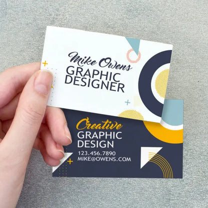 Hand holding front and back business card examples with black, white and yellow graphic design.